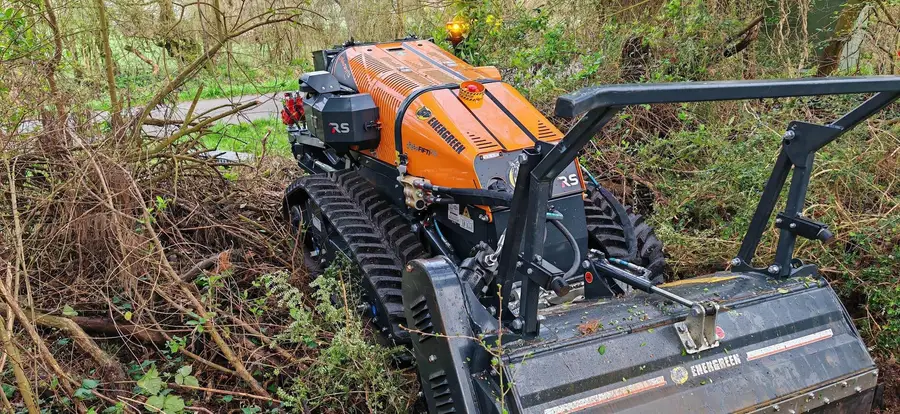 Broyeur forestier engagé dans un mur de ronces à hauteur d'homme, gyrophare allumé